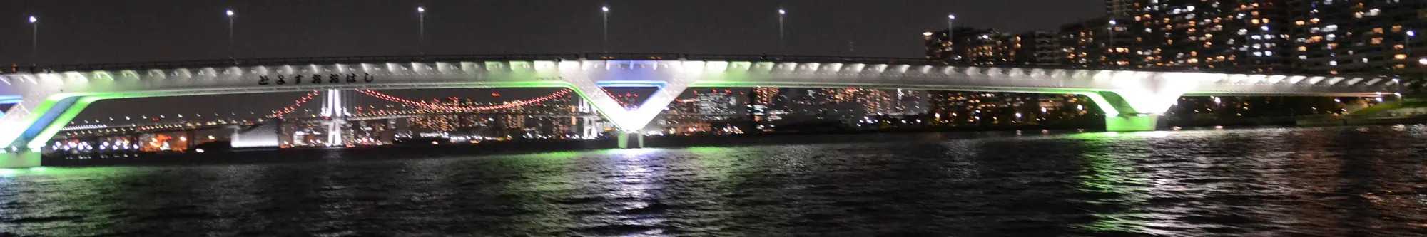 Geceleri karanlık suyun üzerinde yeşil ve beyaz ışıklarla aydınlatılan Toyosu Ōhashi köprüsü; müzenin değil, Toyosu sahil şeridinin genel bir fotoğrafı