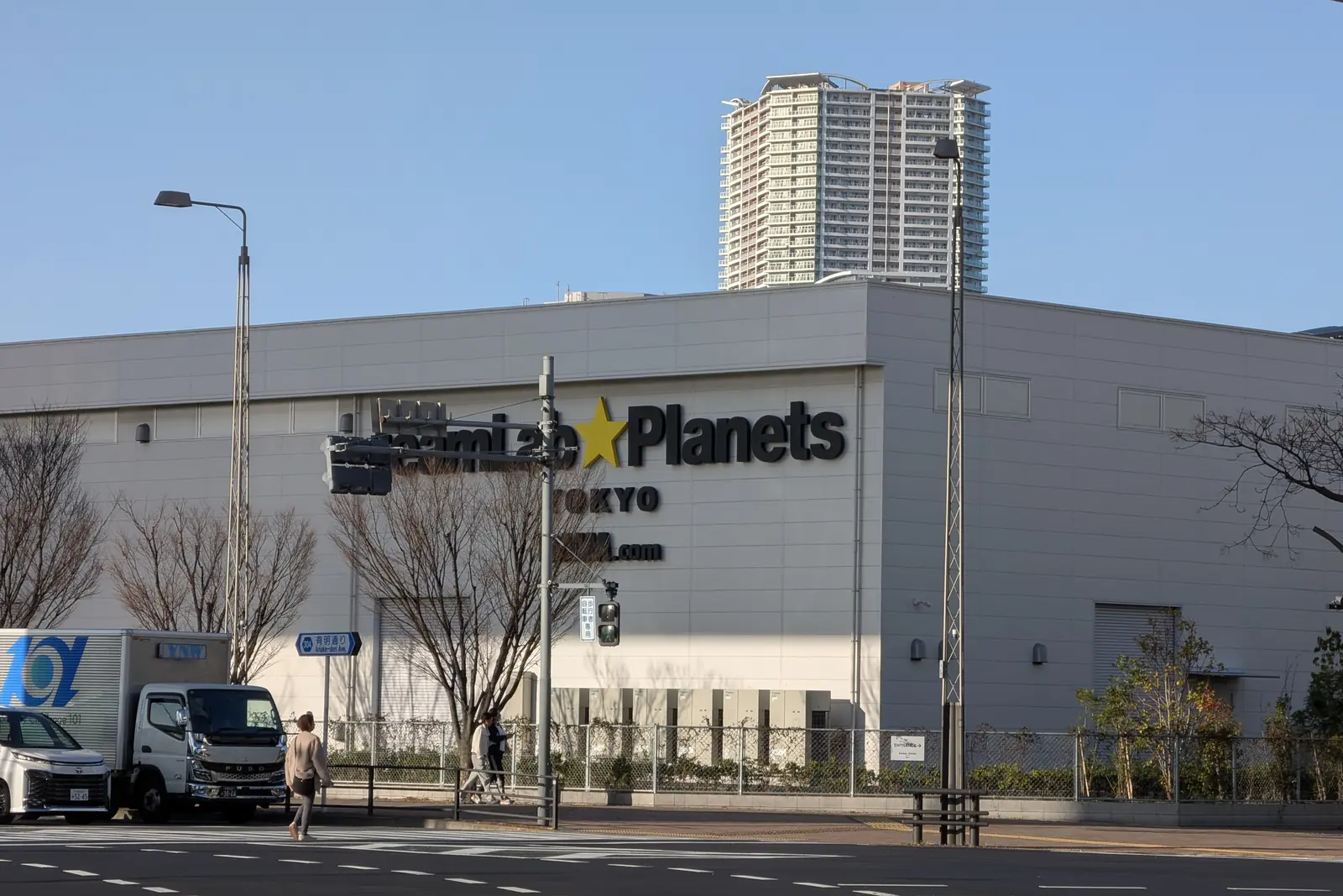 Toyosu'daki teamLab Planets binasının açık bir gökyüzü altındaki gri dış duvarı; cephede müzenin adı ve önünde bir yaya geçidi; sanat eseri görünmeyen bir dış mekân fotoğrafı